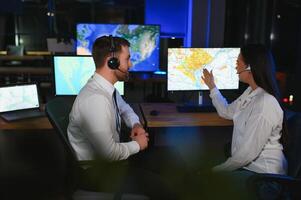 Center of dispatching maintenance. Portrait of cheerful woman and man working via headset microphone while sitting on navigation controller board photo