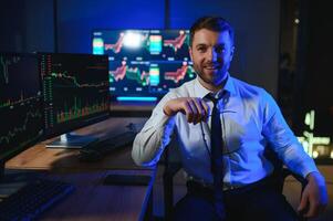 Side view of crypto broker sitting at office table, analyzing market, looking at screen photo