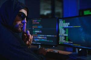 hacker sitting at desk in dark atmosphere. A computer programmer or hacker. Anonymous computer hacker. photo