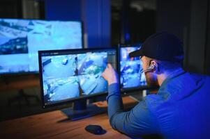 Rear view of security system operator looking at CCTV footage at desk in office photo
