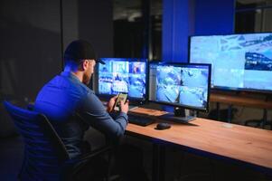 Rear view of security system operator looking at CCTV footage at desk in office photo
