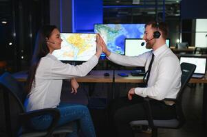 Center of dispatching maintenance. Portrait of cheerful woman and man working via headset microphone while sitting on navigation controller board photo