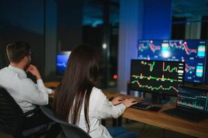 Team of stockbrokers are having a conversation in a dark office with display screens photo