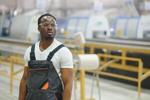 Portrait of industrial engineer. Smiling factory worker with hard hat standing in factory production line photo