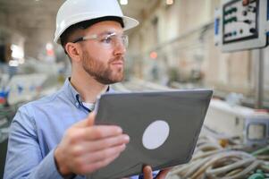 Engineer in hardhat is using a laptop in a heavy industry factory photo