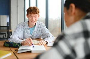 students sit at shared desk making notes studying together at university photo