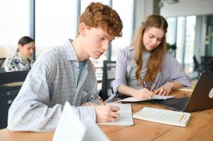 students sit at shared desk making notes studying together at university photo