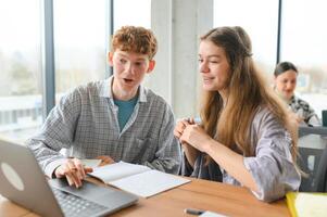students sit at shared desk making notes studying together at university photo