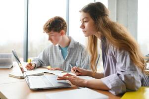 students sit at shared desk making notes studying together at university photo