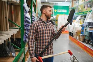 Portrait of a happy young man and customer buying a shovel while shopping at the hardware store photo
