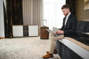 Young businessman working with computer sit on bed in hotel room photo