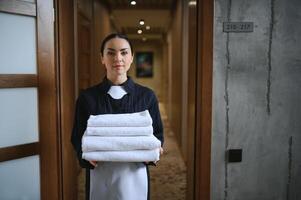The maid is standing in the corridor of the hotel and holding clean towels photo