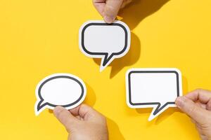 Group of three hands holding a Blank Speech Bubble isolated on yellow background. Mock up template photo