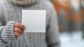 Person Wearing Sweater Holds Blank Square Paper Outdoors in Winter Setting photo