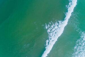 top view of the foam of a wave arriving to the coast, aerial photo with a drone. Summer background