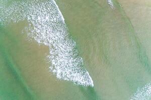 waves on the shore of a turquoise waters beach in the summer, aerial overhead view with drone photo