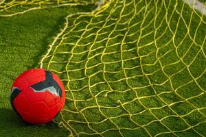 red soccer ball with the yellow net of a goal on an artificial grass football field photo