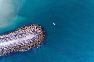 small boat next to a breakwater built with concrete blocks. Top view with drone photo