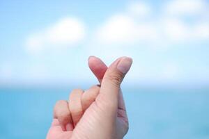 Hand holding a heart shape against the sea and blue sky background. photo