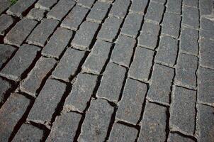 The texture of dark paving stones. Top view of the cobblestone pavement. An old stone sidewalk. The texture of the paving stones. The background is made of cobblestones, the road is made of cobbleston photo