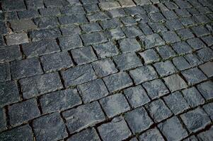 The texture of dark paving stones. Top view of the cobblestone pavement. An old stone sidewalk. The texture of the paving stones. The background is made of cobblestones, the road is made of cobbleston photo