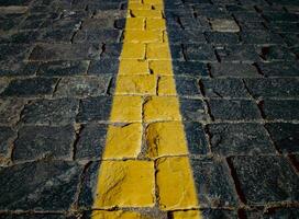The texture of dark paving stones. The yellow stripe. An old stone sidewalk. The texture of the paving stones. The background is made of cobblestones, the road is made of cobblestones. photo