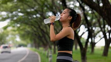 A woman is drinking water while walking on a road photo