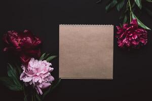 Beautiful peonies in dark colors and notebook. Black Floral background. Soft focus, copy space photo