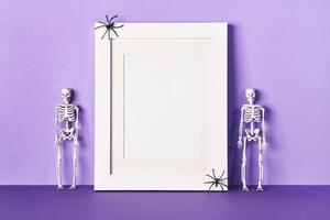 Halloween composition with frame and skeletons on table wall background. Greeting card template photo