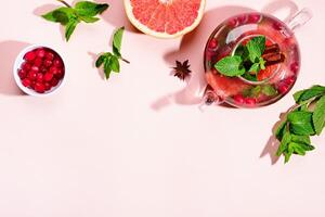 Immunity boosting drink. Mint Tea with cranberries, grapefruit and spices in glass teapot on pink table, trendy shadows photo