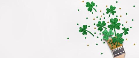Creative St. Patricks Day concept made with paint brush and green glitter shamrocks and confetti. Banner format photo