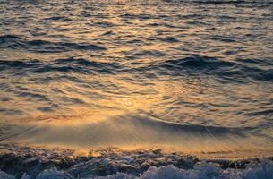 Abstract photo of surface water of sea or ocean at sunset time with golden light tone.