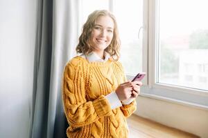 Joyful Woman Using Smartphone at Home. Smiling woman using her phone at home, enjoying online shopping and texting. Capturing a moment of happiness and modern lifestyle in a cozy indoor setting. photo