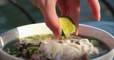 Add Lime to Pho Soup close-up top view. female hands add sauce to a bowl of pho bo soup. video
