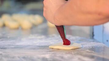 Female hands apply raspberry jam to cookies from a pastry bag. Preparation of confectionery products. A female confectioner applies jam to cookies using a pastry bag. Close up video