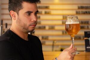 Young latin tasting craft beer in a pub, observing the color and hops in the lager. photo