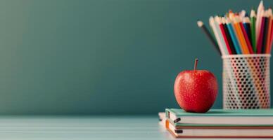 Red Apple on Stack of Notebooks With Colorful Pencils in Container Against a Green Background photo