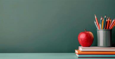 Red Apple on Stack of Notebooks With Colorful Pencils in Container Against a Green Background photo