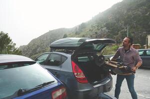 Man taking a break with a mountain longboard adventure, unloading from a car photo