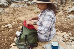 Woman exploring nature and checking her backpack for supplies while hiking in a rocky terrain photo