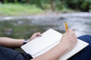 Cropped image of man writing in notebook ideas and enjoying nature in the park, while writing a book at campsite. photo