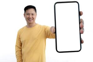 Online Offer. Cheerful Asian man showing a large smartphone with a blank white screen and making a happy gesture looking at the camera. A man in his 40s suggests a new mobile app or website. photo