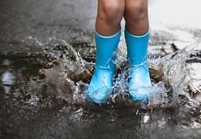 Child wearing blue rain boots jumping into a puddl photo