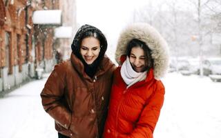 Two happy female friends enjoying snowing weather outdoors in winter during Christmas holidays photo