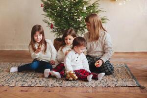 Happy four little siblings, three sisters and small brother in warm knitted sweaters gathered around fir-tree photo