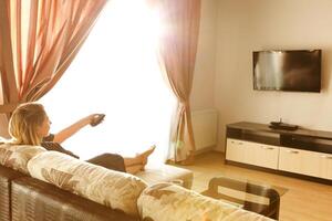 Back view of young woman watching tv while resting and sitting on sofa in living room photo