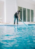 Young man cleaning a swimming pool with suction hose. Swimming pool cleaning and maintenance service photo