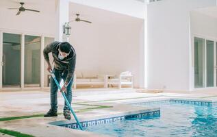 Worker cleaning a home pool with a vacuum hose. Man cleaning swimming pool with a suction hose photo