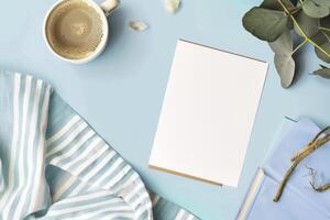 Blank paper sheet, cup of coffee on blue background. Top view with copy space photo