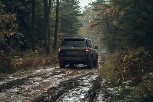 Full size SUV parked at an off road trailhead with rugged terrain and muddy tracks leading into dense forest photo